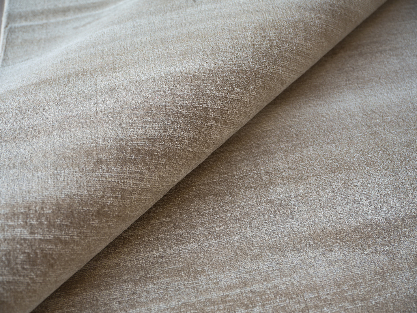Beige velvet-like upholstery fabric close-up with plush nap and folded edge, ideal for sofas or cushions.