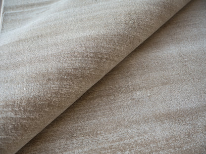 Beige velvet-like upholstery fabric close-up with plush nap and folded edge, ideal for sofas or cushions.