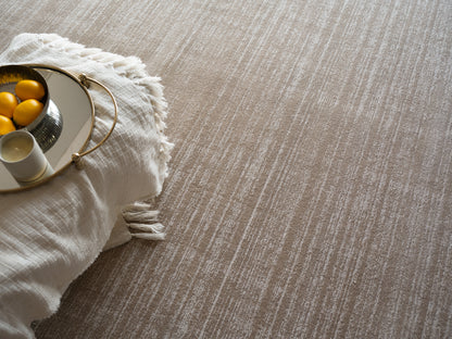 Beige textured rug with white fringed throw; round gold-trimmed mirror tray holding lemons & a white cup.