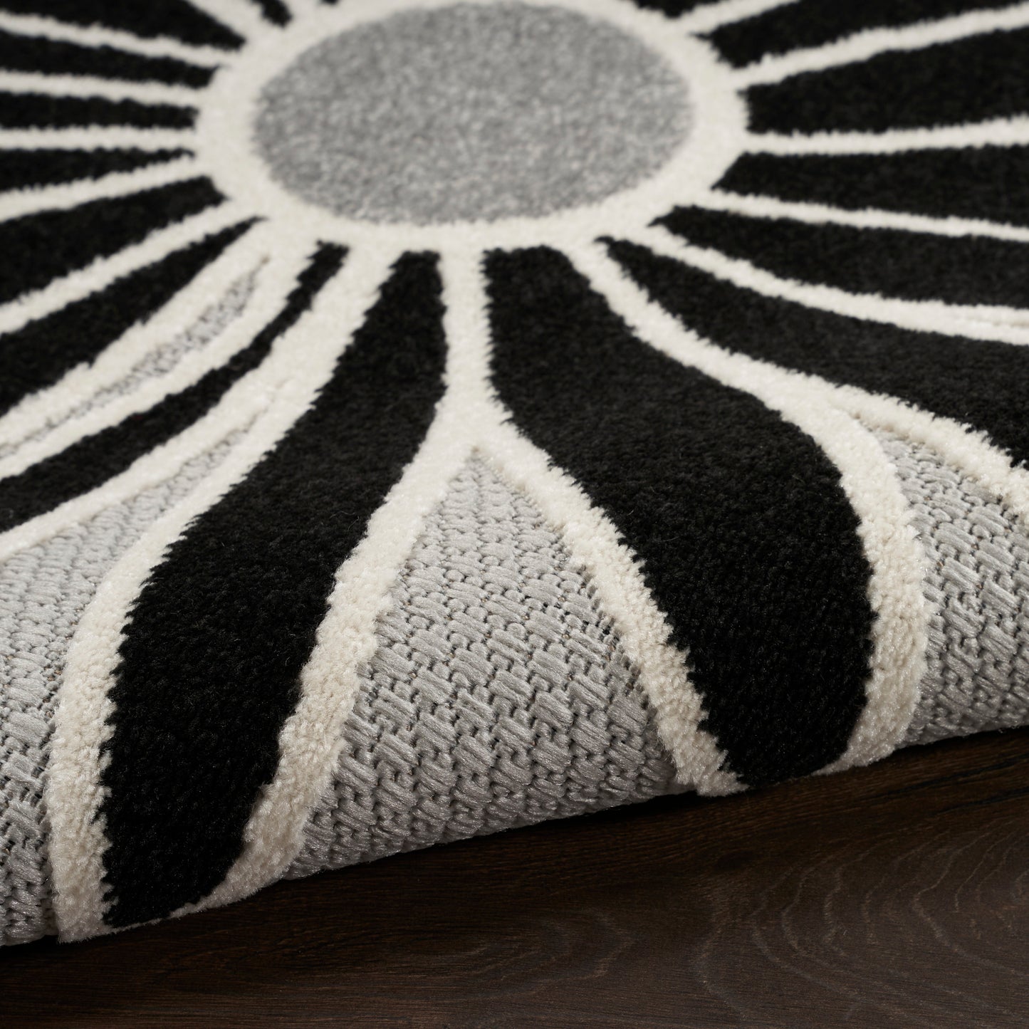 Sunburst rug with black, white and grey radiating stripes; soft textured pile and grey center, on dark wood floor.