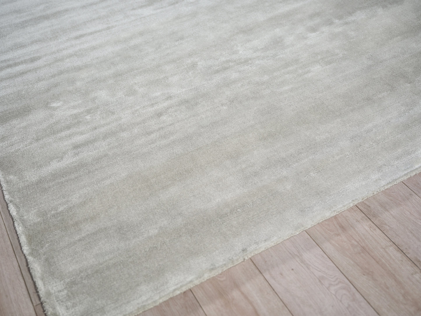 Light beige textured area rug laid over pale wood flooring.