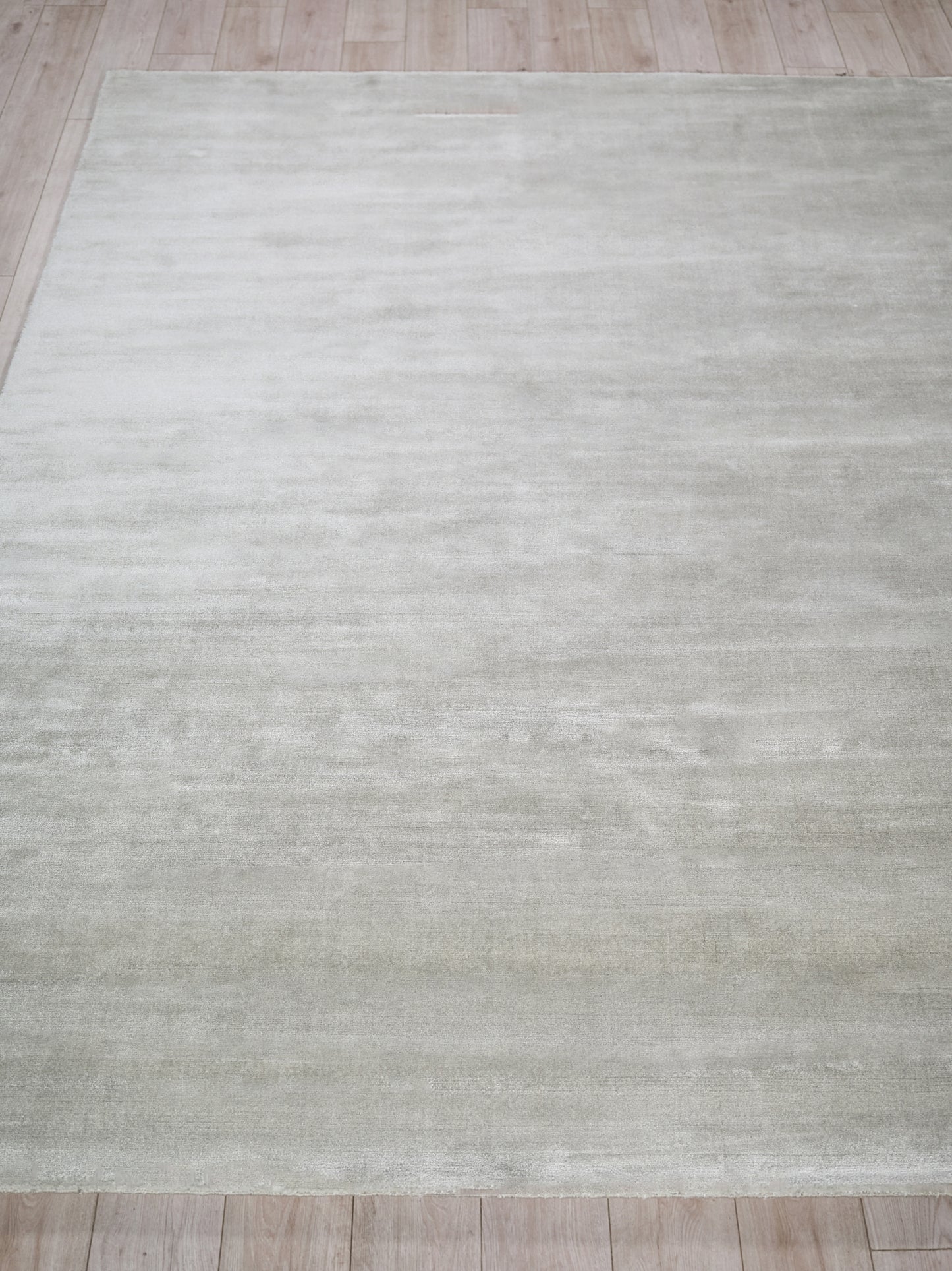 Rectangular light gray rug with subtle tonal texture on a pale wooden floor.