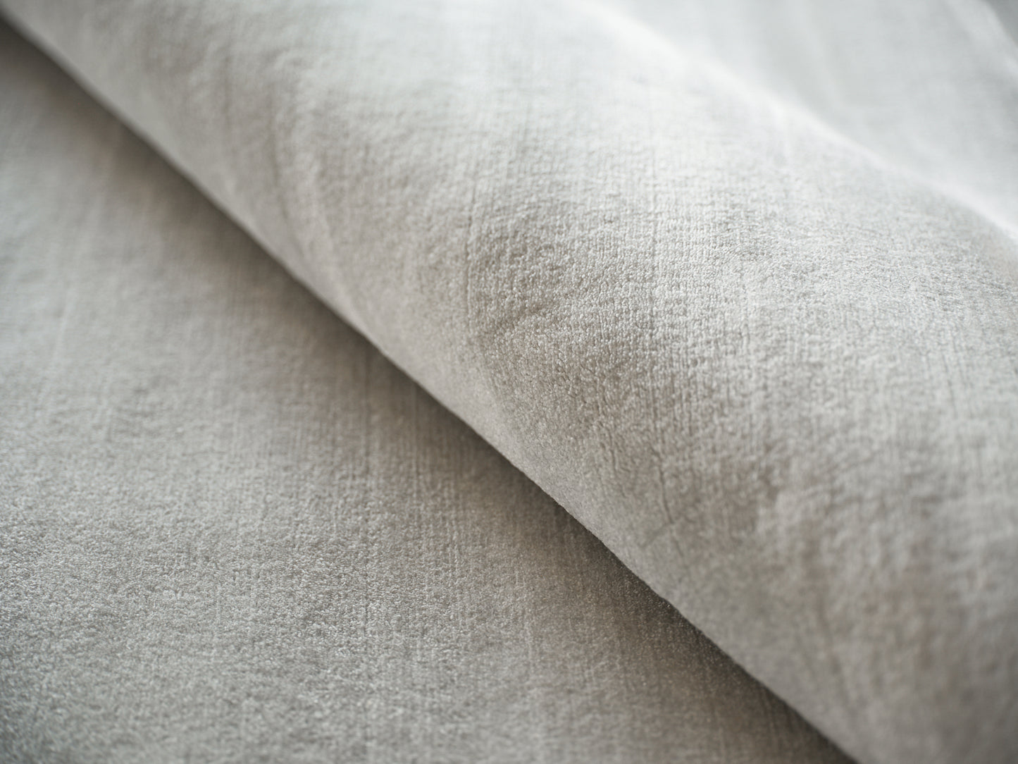 Light gray velvet-like fabric close-up with a fold; soft, plush upholstery or throw material.