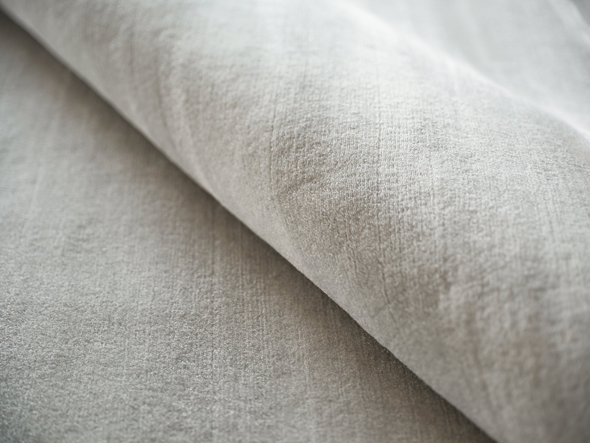 Light gray velvet-like fabric close-up with a fold; soft, plush upholstery or throw material.