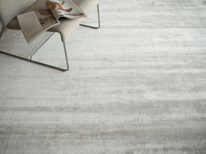 Light gray textured area rug with subtle horizontal pattern; beige modern lounge chair with metal legs nearby.