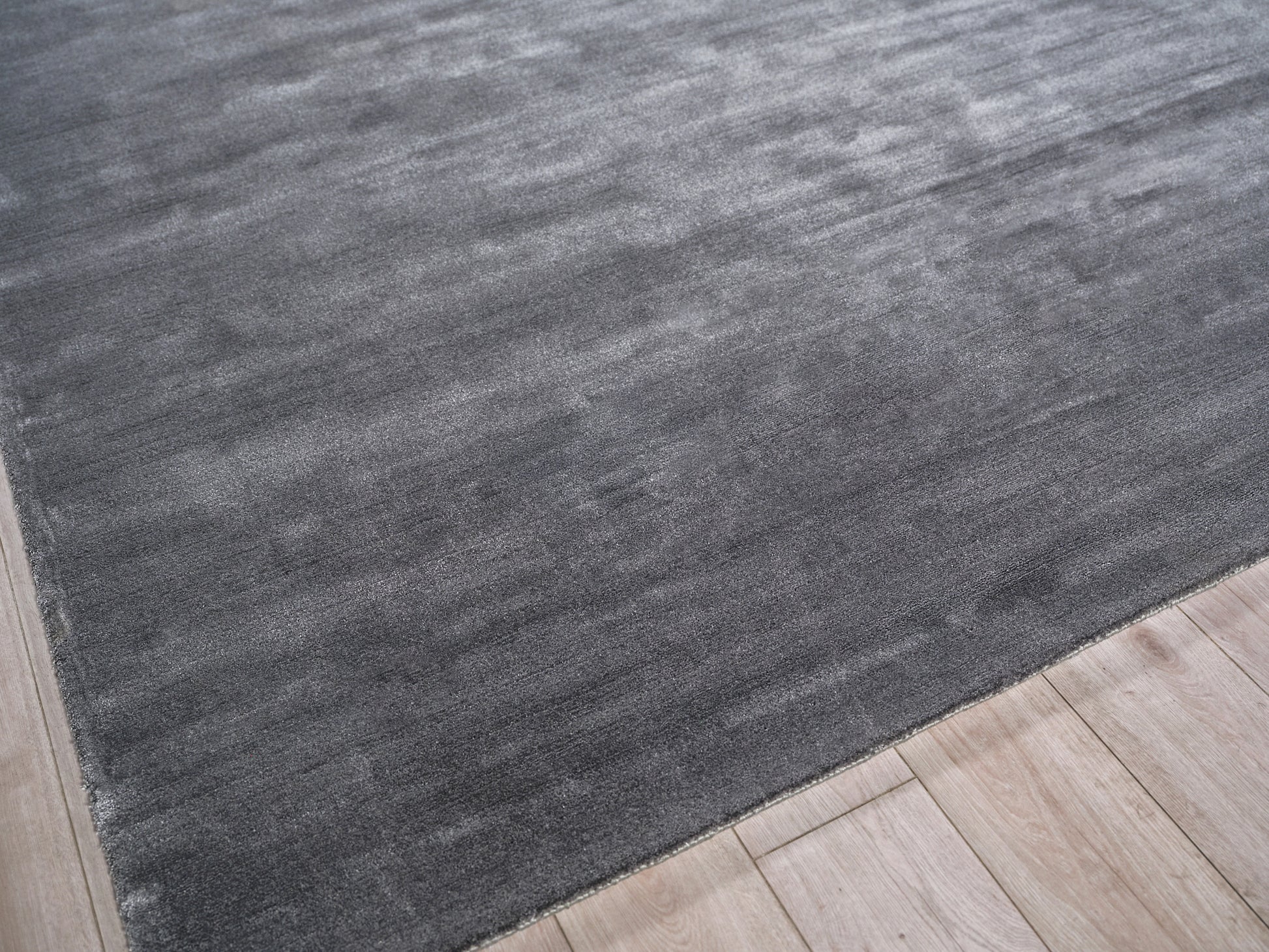 Dark charcoal gray hand loomed area rug on a light wood floor; modern minimalist style.