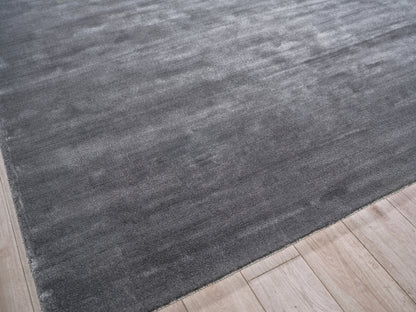 Dark charcoal gray hand loomed area rug on a light wood floor; modern minimalist style.