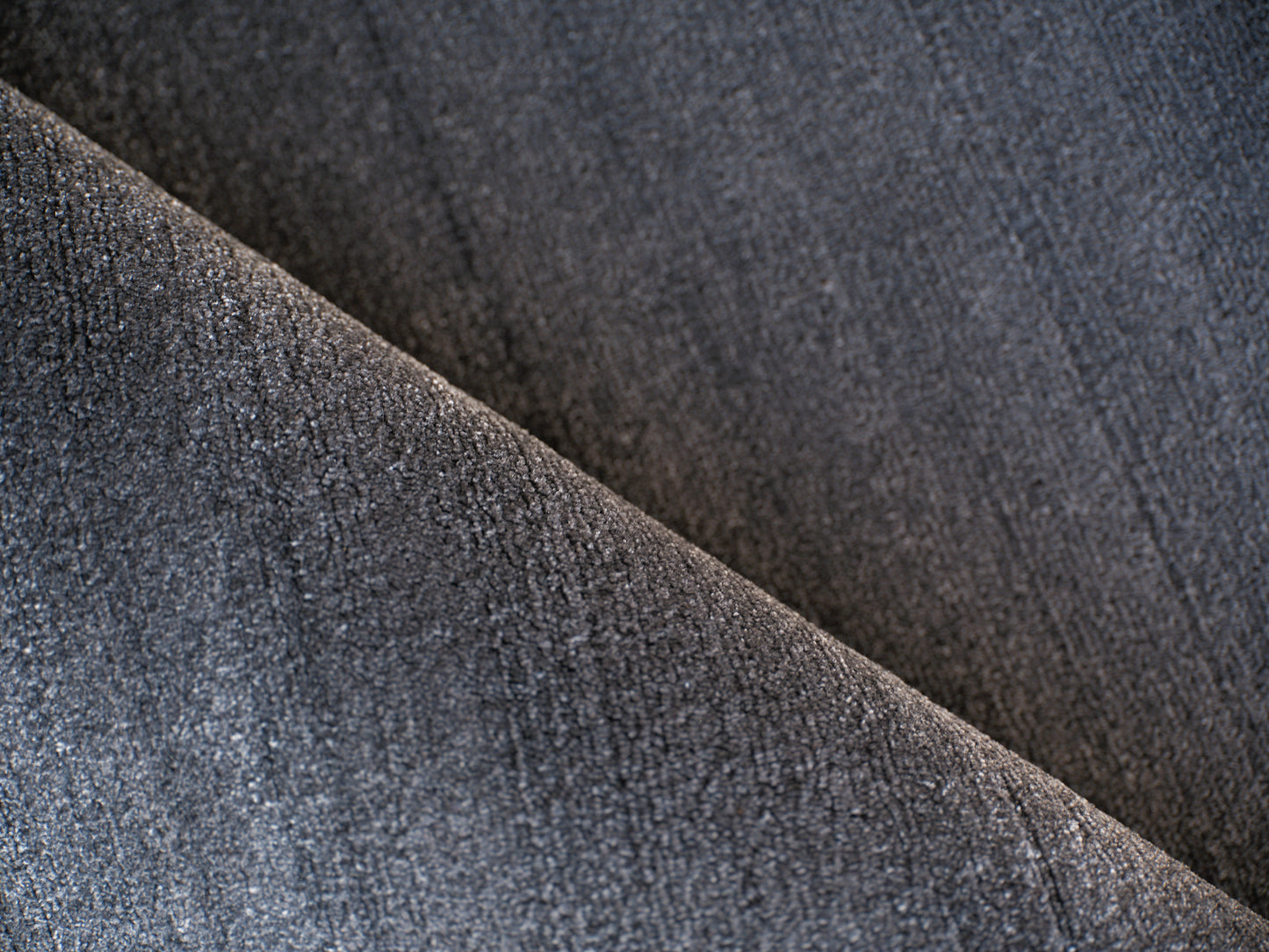 Dark grey rug close-up showing weave, diagonal fold and soft texture.