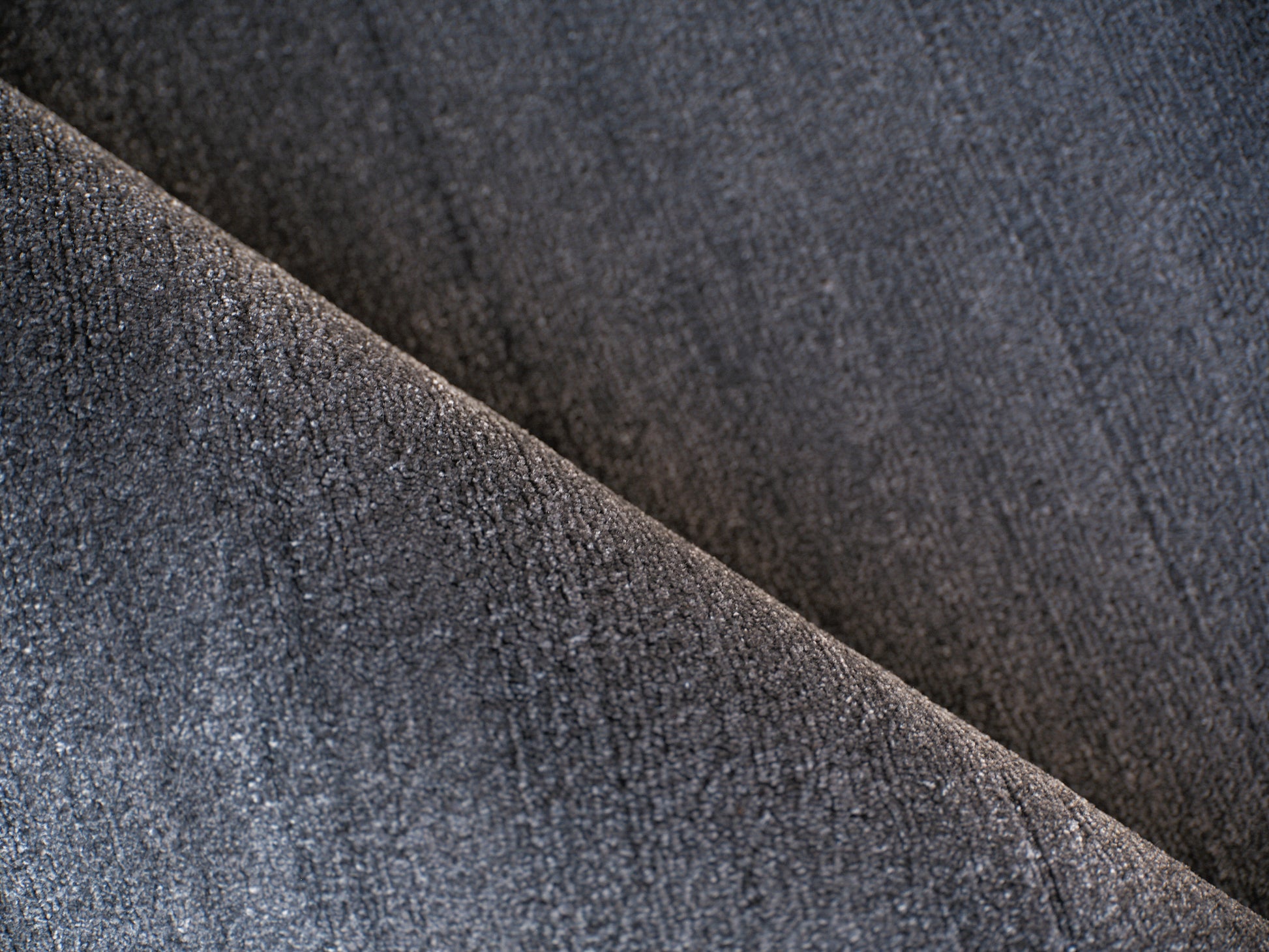 Dark grey rug close-up showing weave, diagonal fold and soft texture.
