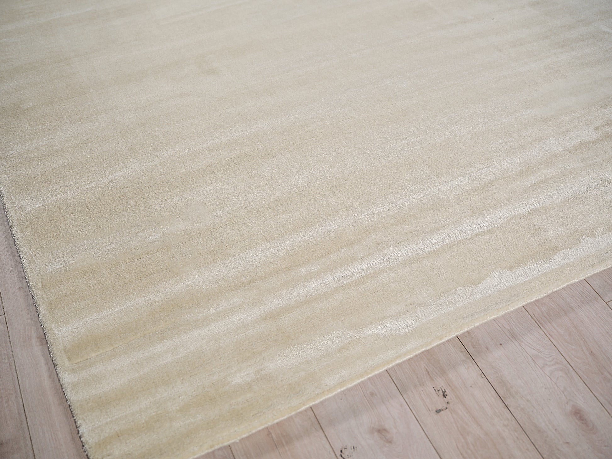 Beige hand-loomed rug with soft texture & subtle banding on light wood floor, rectangular & minimalist.