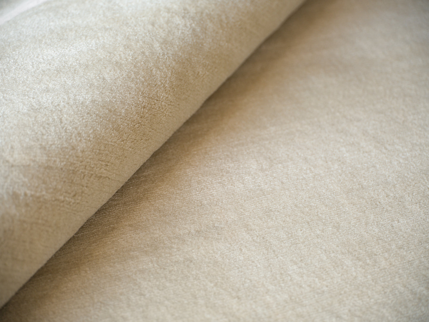 Beige rug close-up showing a suede-like pile, rolled edge and soft nap.