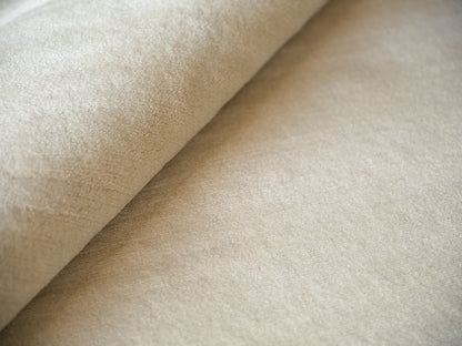 Beige rug close-up showing a suede-like pile, rolled edge and soft nap.