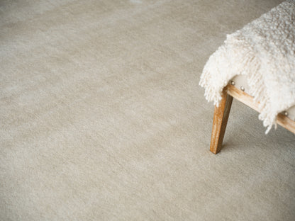 Beige hand-loomed rug (4' x 6') with a small wooden stool and a fluffy cream throw draped over the stool.