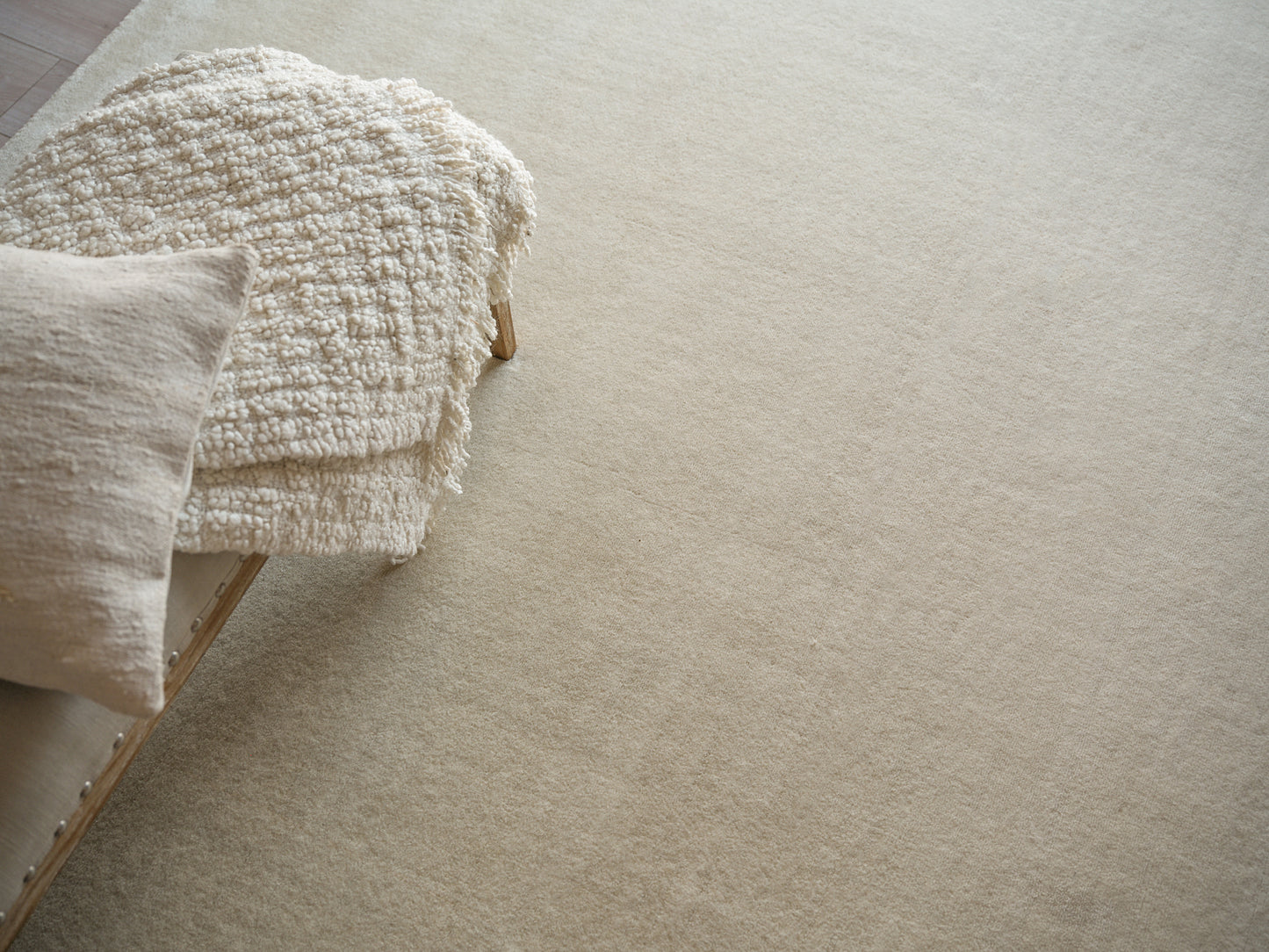 Cream textured rug in neutral beige tones on a soft beige floor, with a beige pillow and a light wood chair nearby.