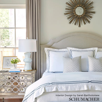 Soft gray upholstered bed with white and blue bedding, sunburst mirror, mirrored nightstand and pale blue lamp.