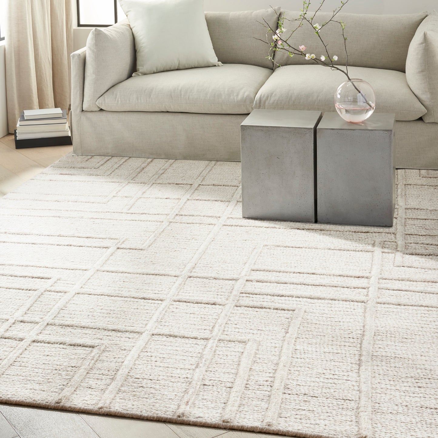 Neutral living room with a cream geometric area rug, light gray sofa, & square metal side tables topped with a glass vase.