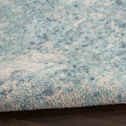 Blue-toned plush area rug with subtle beige pattern, edge folded over dark wood floor.
