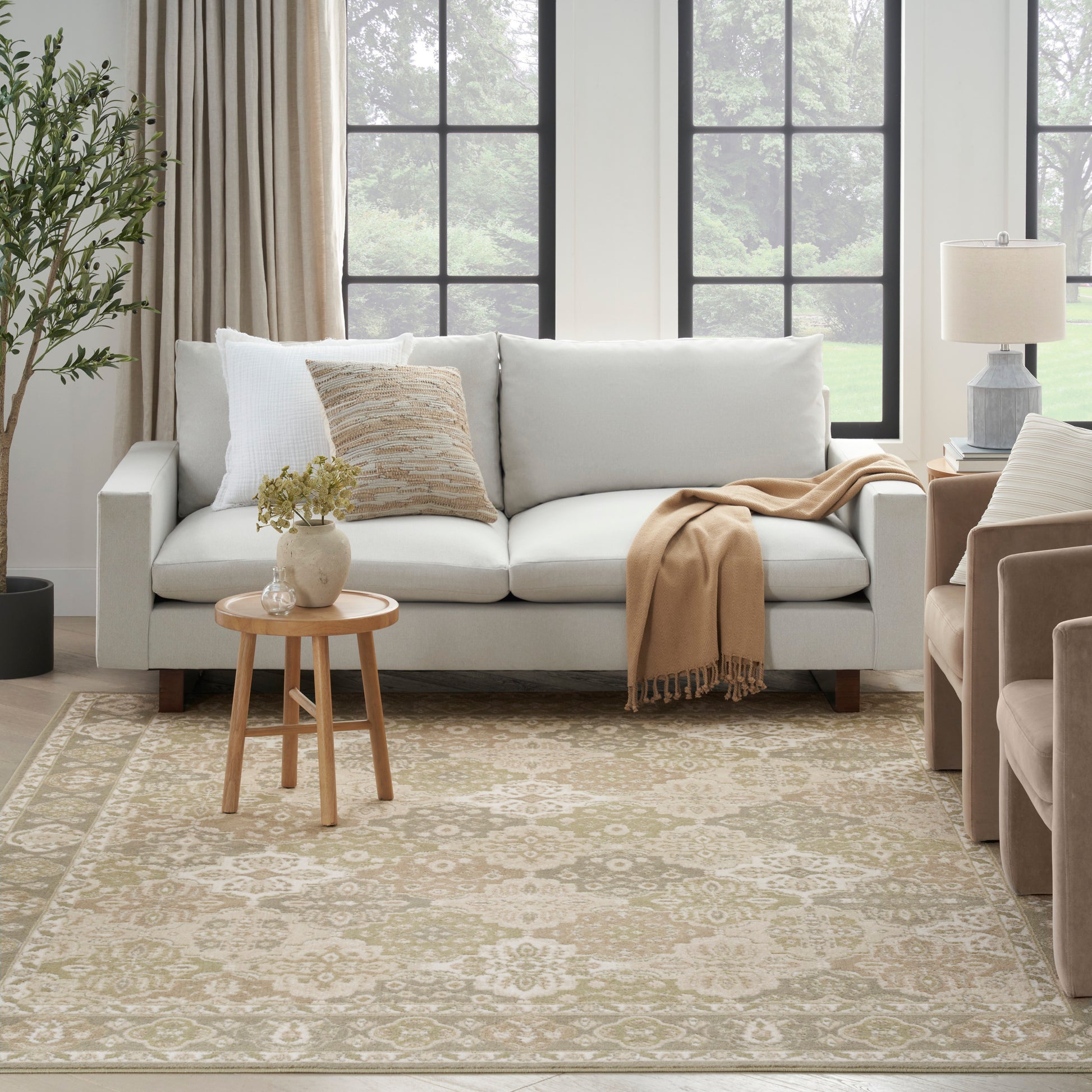 Cozy living room scene with a light gray sofa, beige throw, cream patterned rug, round wooden coffee table, and potted plant.