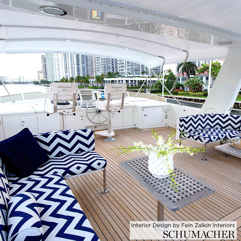 Luxury yacht deck with navy and white chevron cushions, wooden plank floor, lattice-top table with vase, helm chairs and skyline.