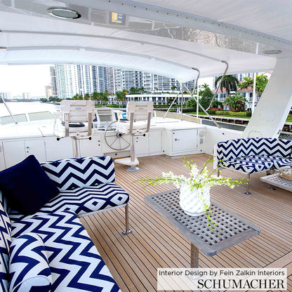 Luxury yacht deck with navy and white chevron cushions, wooden plank floor, lattice-top table with vase, helm chairs and skyline.