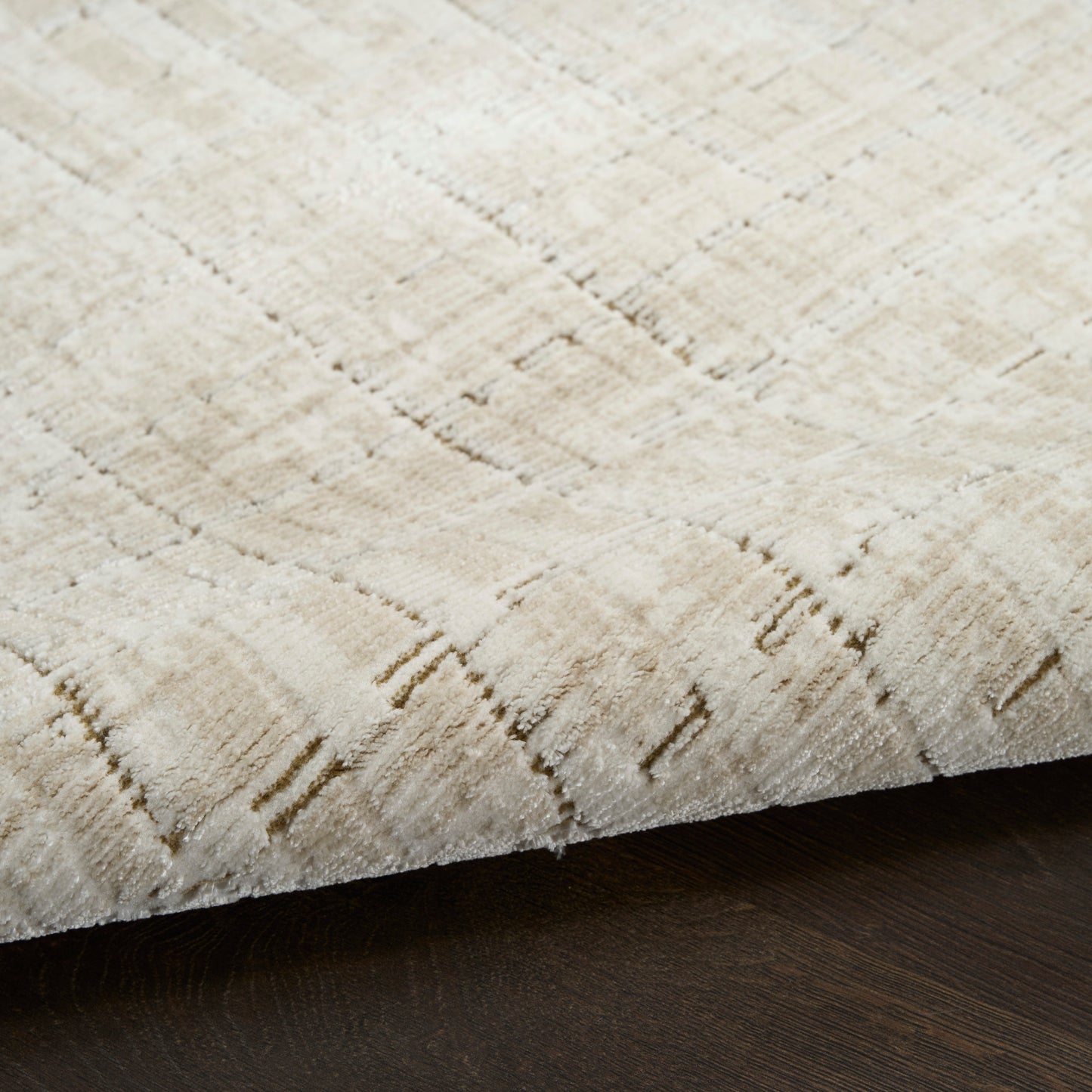 Beige area rug with subtle linear pattern and soft texture, edge resting on dark wooden floor.