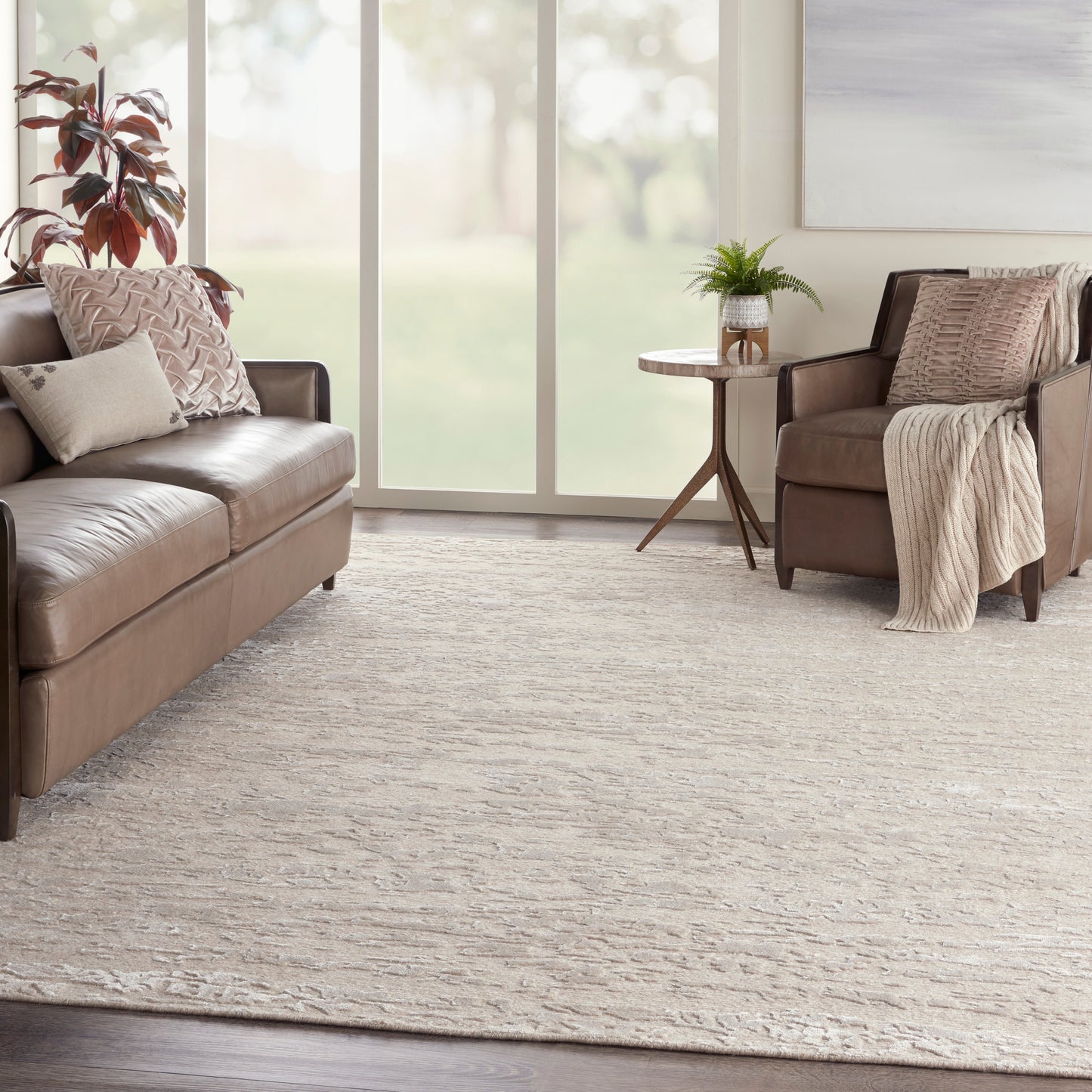 Beige textured area rug in a living room with brown leather sofas, neutral pillows, a cozy throw, and a plant on a small side table.