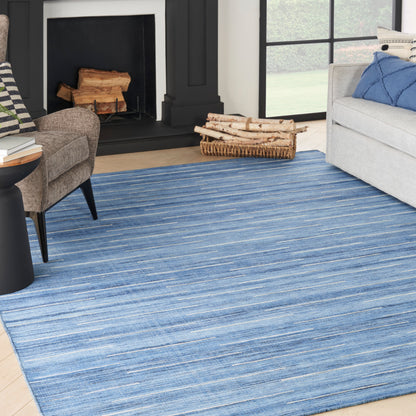 Blue striped area rug on a light wood floor in a modern living room with a gray sofa, a dark chair, a fireplace, and a firewood basket.