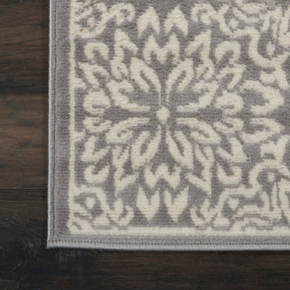 Gray and ivory area rug with a central ornate medallion pattern, plush low-pile, bordered edge on dark wood floor.
