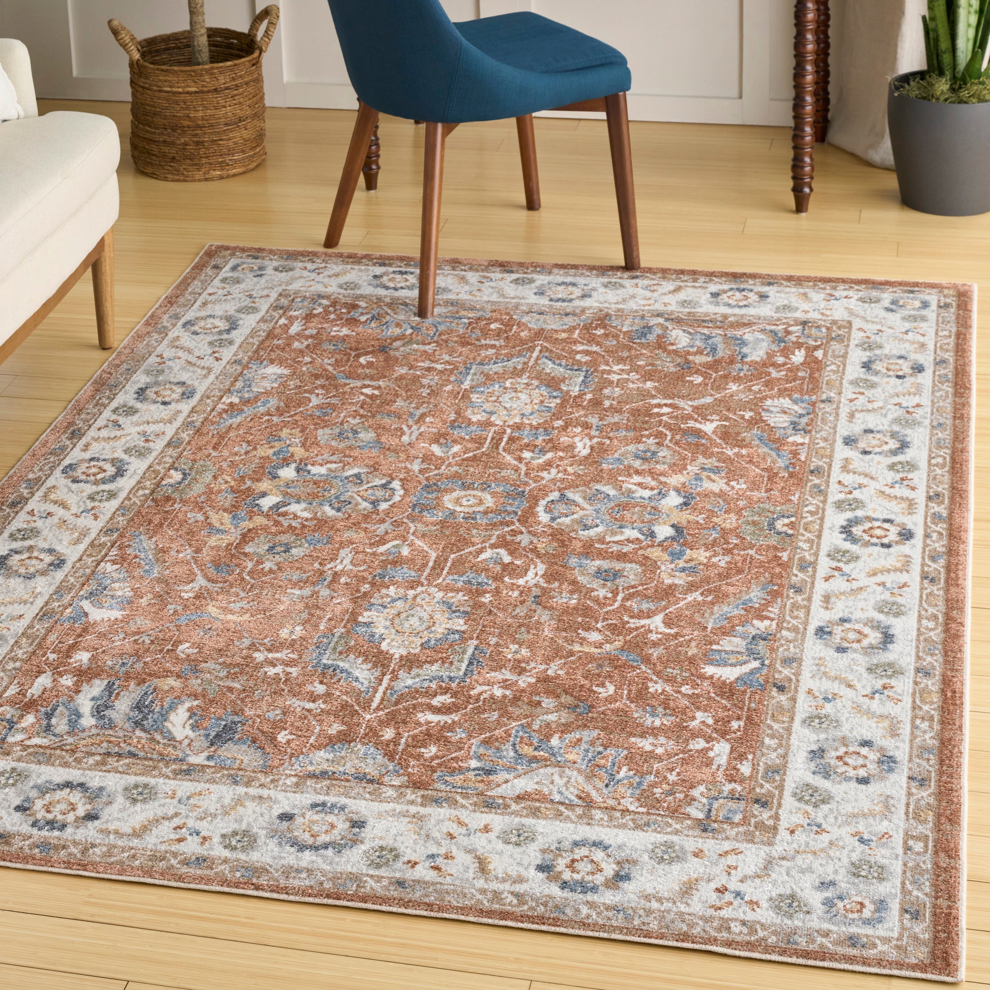 Rectangular oriental rug with rust-orange center and blue/cream floral border on a wooden living room floor.