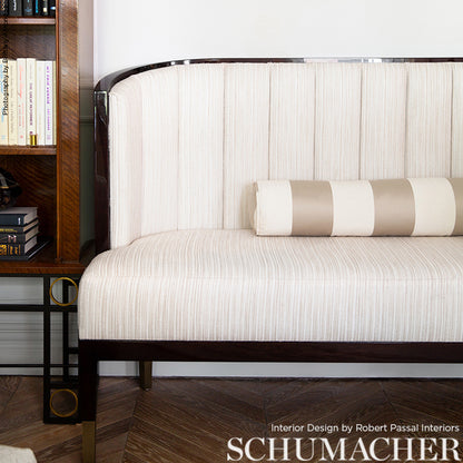 Cream, channel-tufted upholstery sofa with dark wood frame and chrome trim, beige striped bolster, in a bookshelf room.