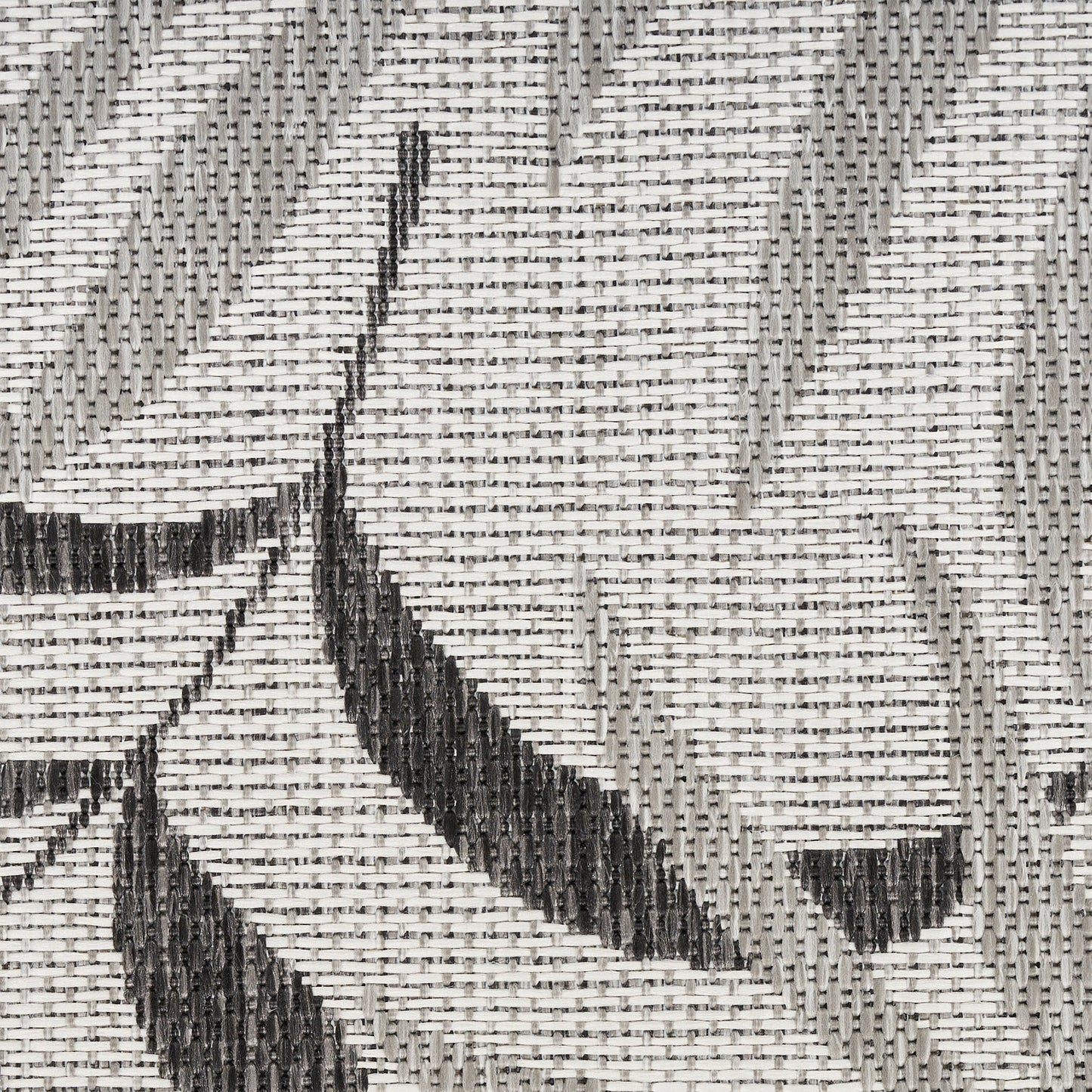 Close-up of grayscale woven rug with black geometric leaf/arrow patterns and alternating light and dark gray threads.