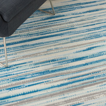 Close-up of a blue-gray striped rug with white and blue bands under a dark upholstered chair with metal legs.