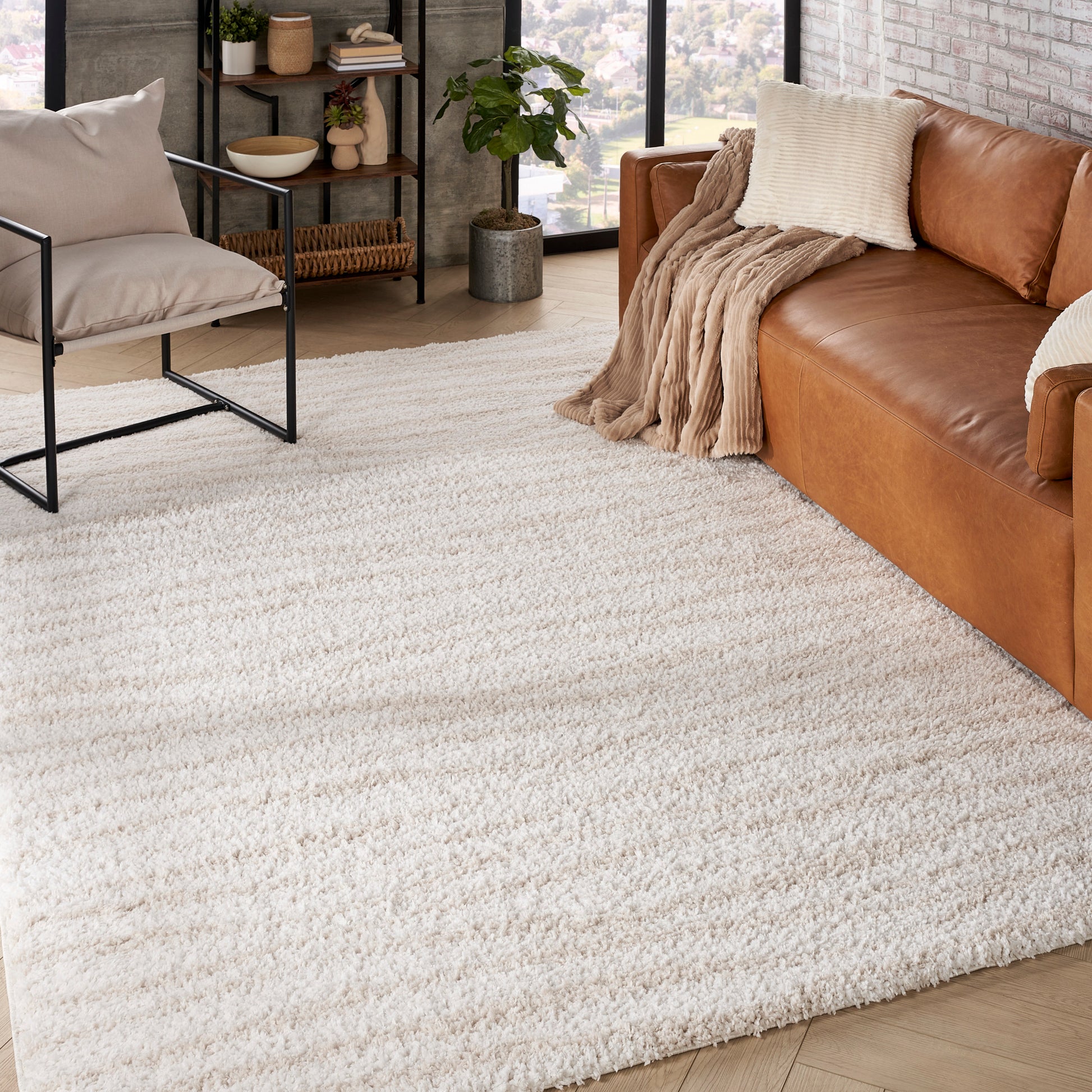 Cream shag area rug anchors a modern living room with a tan leather sofa, beige throw, black metal chair, and open shelving.