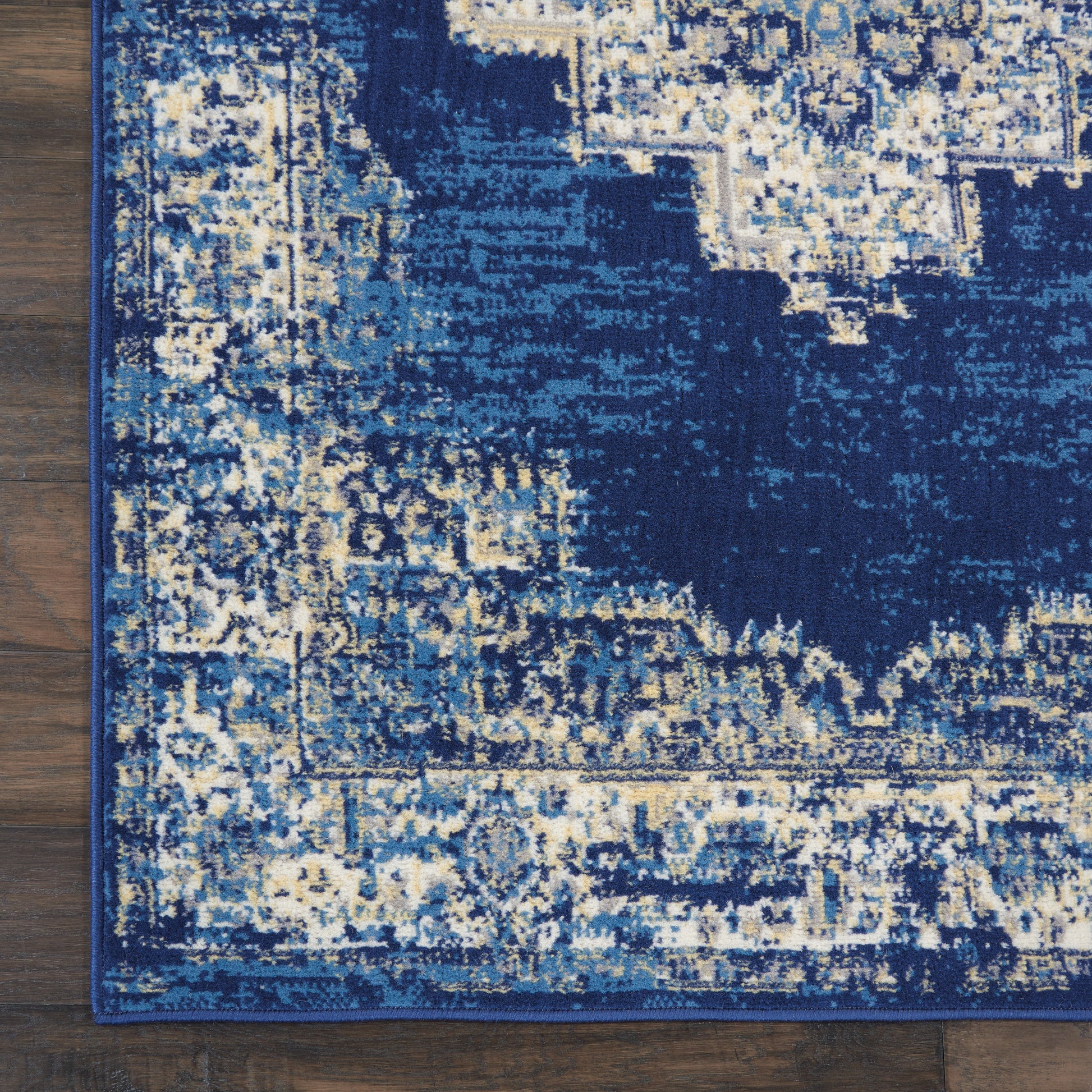 Dark navy distressed area rug with ivory and light-blue motifs and ornate border on wooden floor.