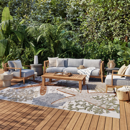 Leaf-pattern outdoor rug on a wooden deck amid lush tropical plants; 9' x 12'.