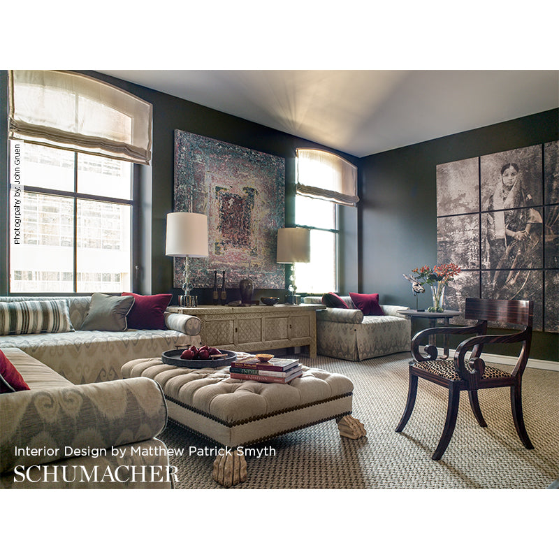 Elegant living room with dark green walls, tufted beige ottoman, patterned sofas, red cushions, and large abstract wall art.