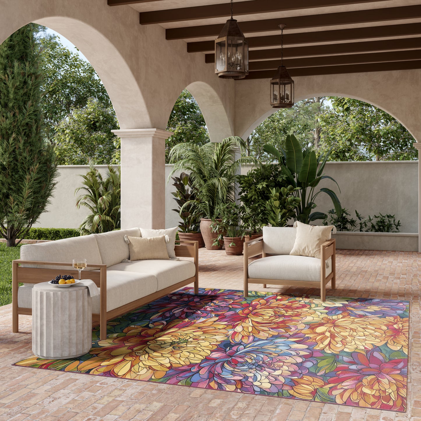 Outdoor patio with beige cushioned wooden sofas, vibrant floral rug, potted tropical plants, arches & lanterns.