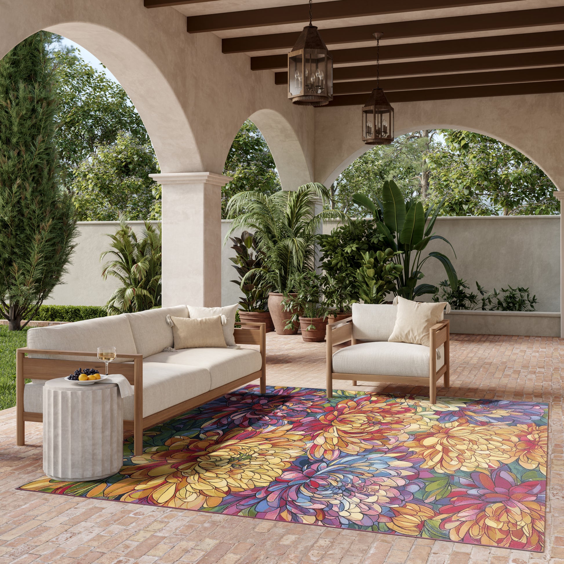 Outdoor patio with beige cushioned wooden sofas, vibrant floral rug, potted tropical plants, arches & lanterns.