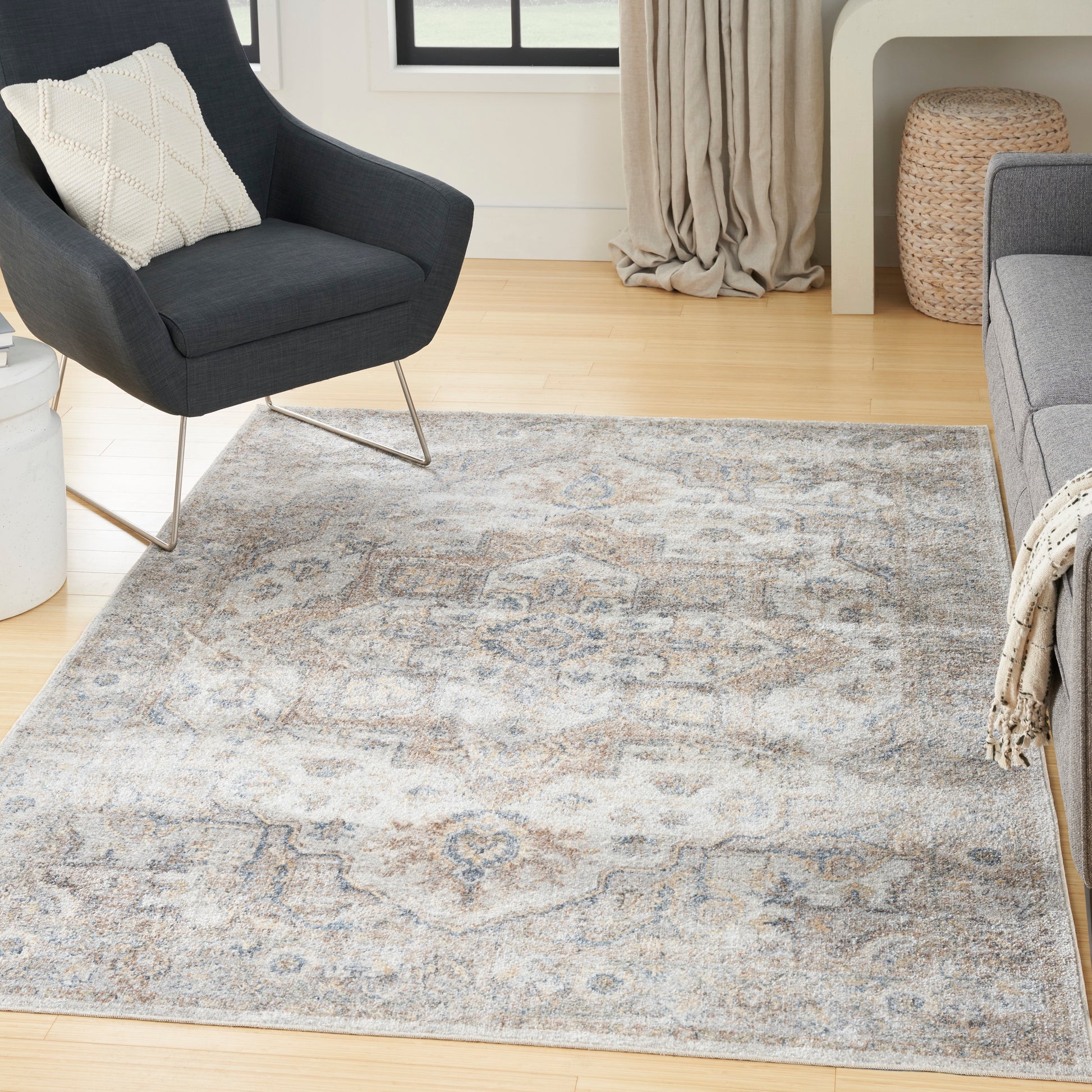Dark gray mid-century armchair with metal legs beside a blue-gray oriental patterned area rug in a bright living room.