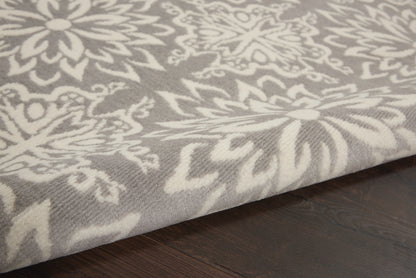 Close-up of a gray-white damask-pattern rug on dark wood floor with ornate floral motifs.