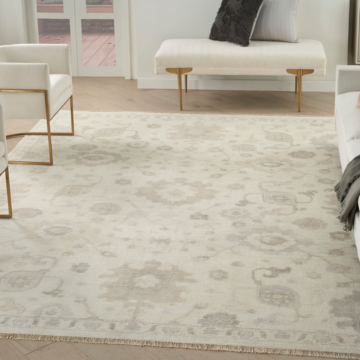 Soft ivory area rug with subtle gray damask pattern in a modern living room; white seating with gold metal legs.