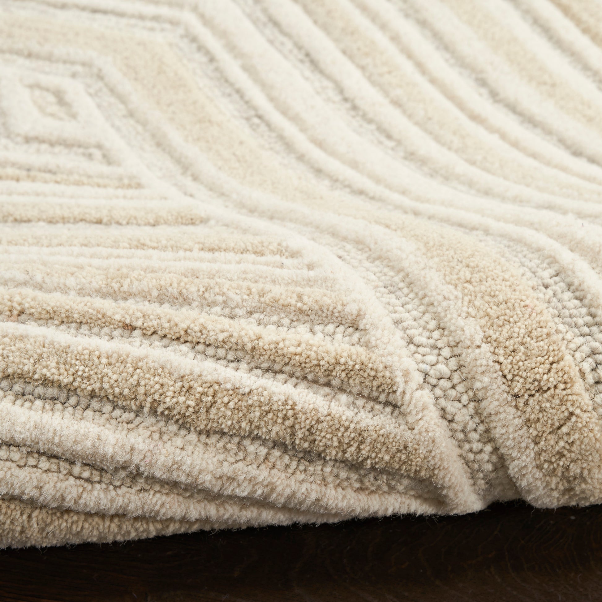 Cream beige plush rug with a raised geometric pattern and soft texture, draped on dark wood floor (5' x 7').