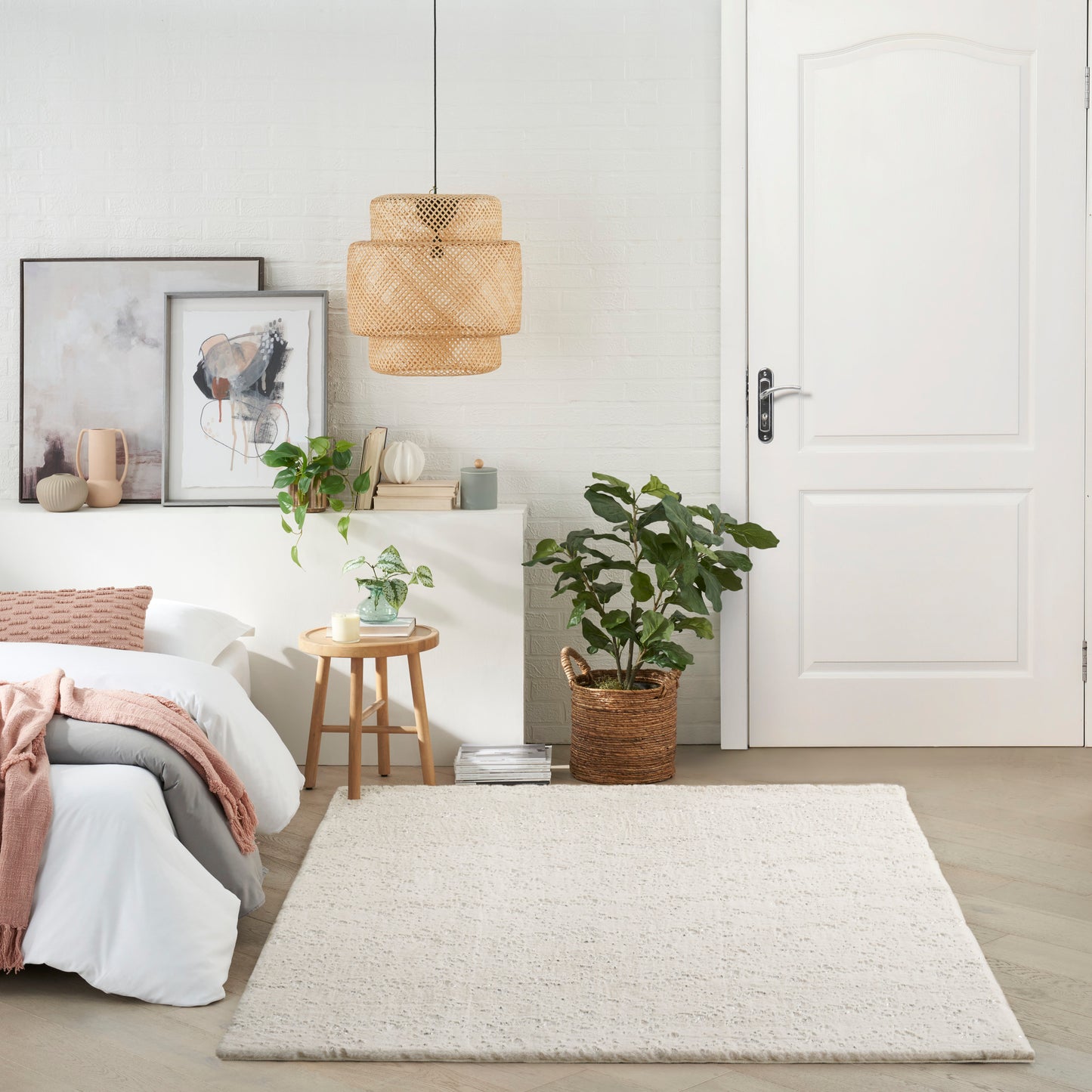 Bright modern bedroom with white walls, bed with white linens and pink throw, woven pendant light, art, and potted plants.