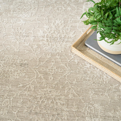 Beige damask rug with a soft off-white pattern; a natural woven tray on the rug holds a potted fern & books.