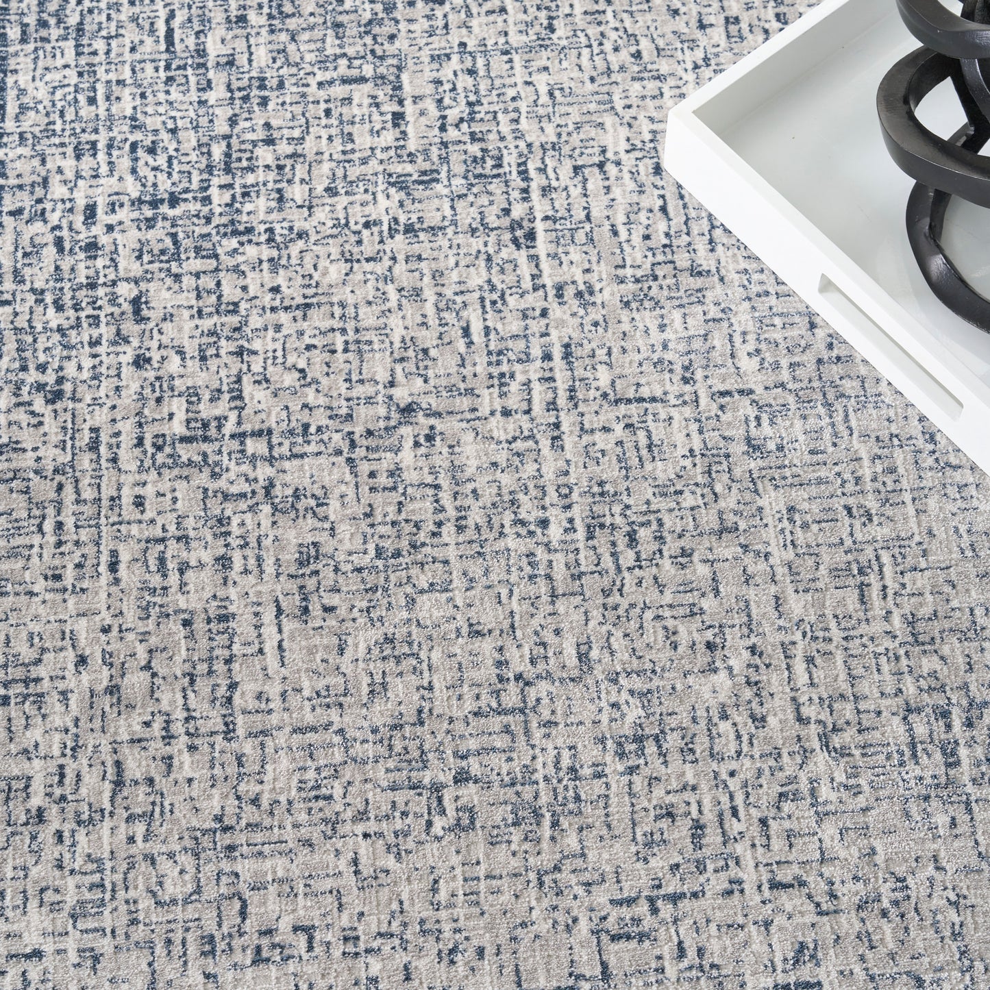 Blue and cream woven area rug with abstract geometric pattern; white tray with black coil decor visible.