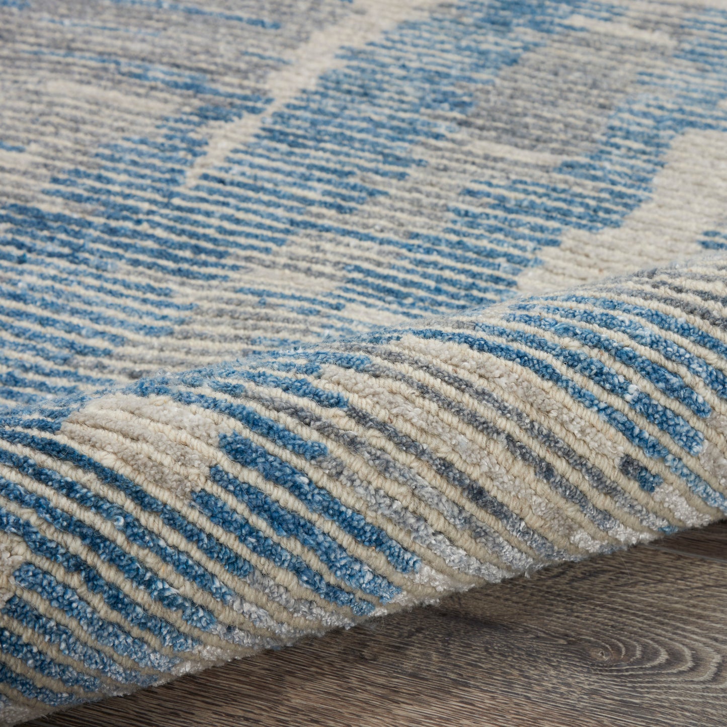 Close-up of blue and beige striped textured rug with soft pile on wooden floor.
