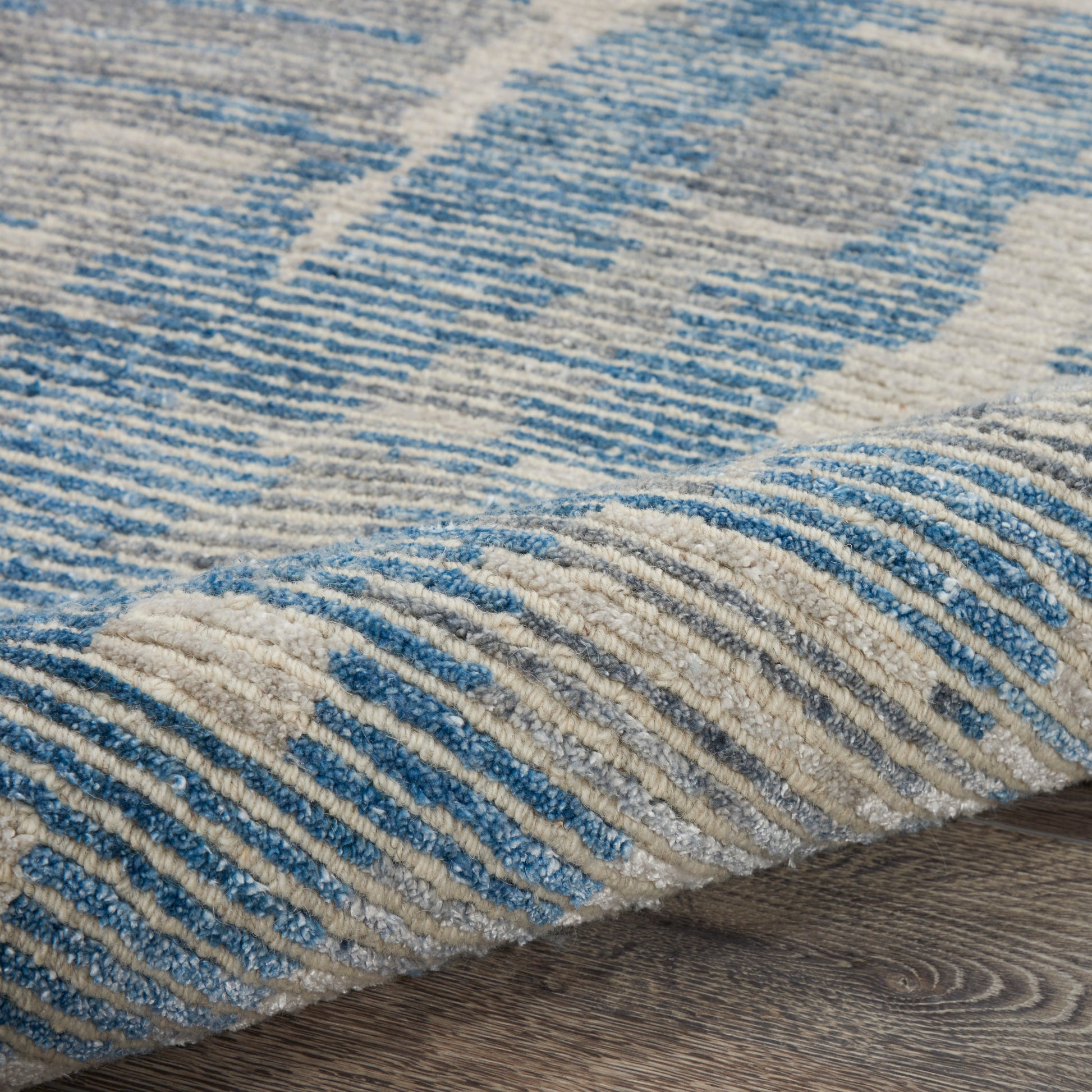 Close-up of blue and beige striped textured rug with soft pile on wooden floor.