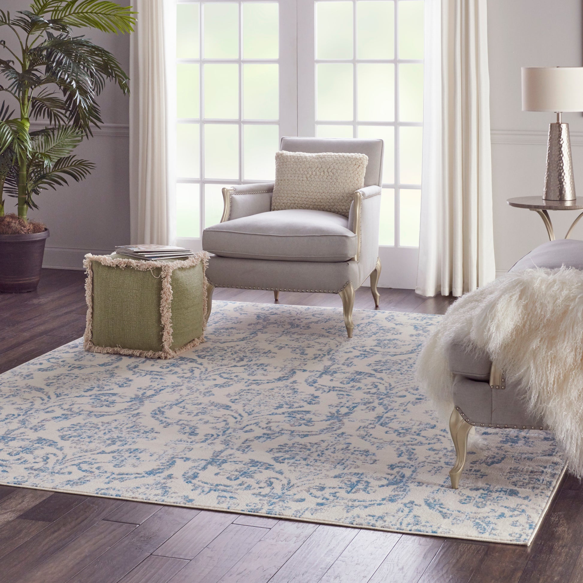Blue floral area rug in a bright living room, with a soft gray armchair with a beige cushion beside a fringed green ottoman.