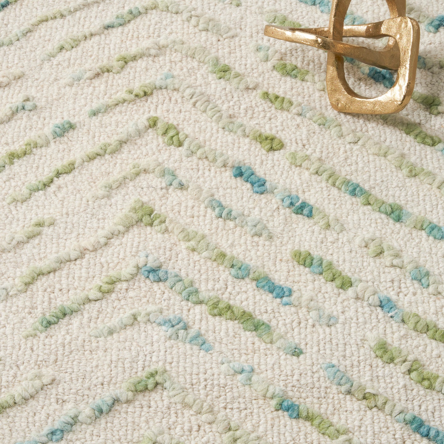 Beige textured area rug with pastel green and blue dashed lines; gold metal belt buckle on top.