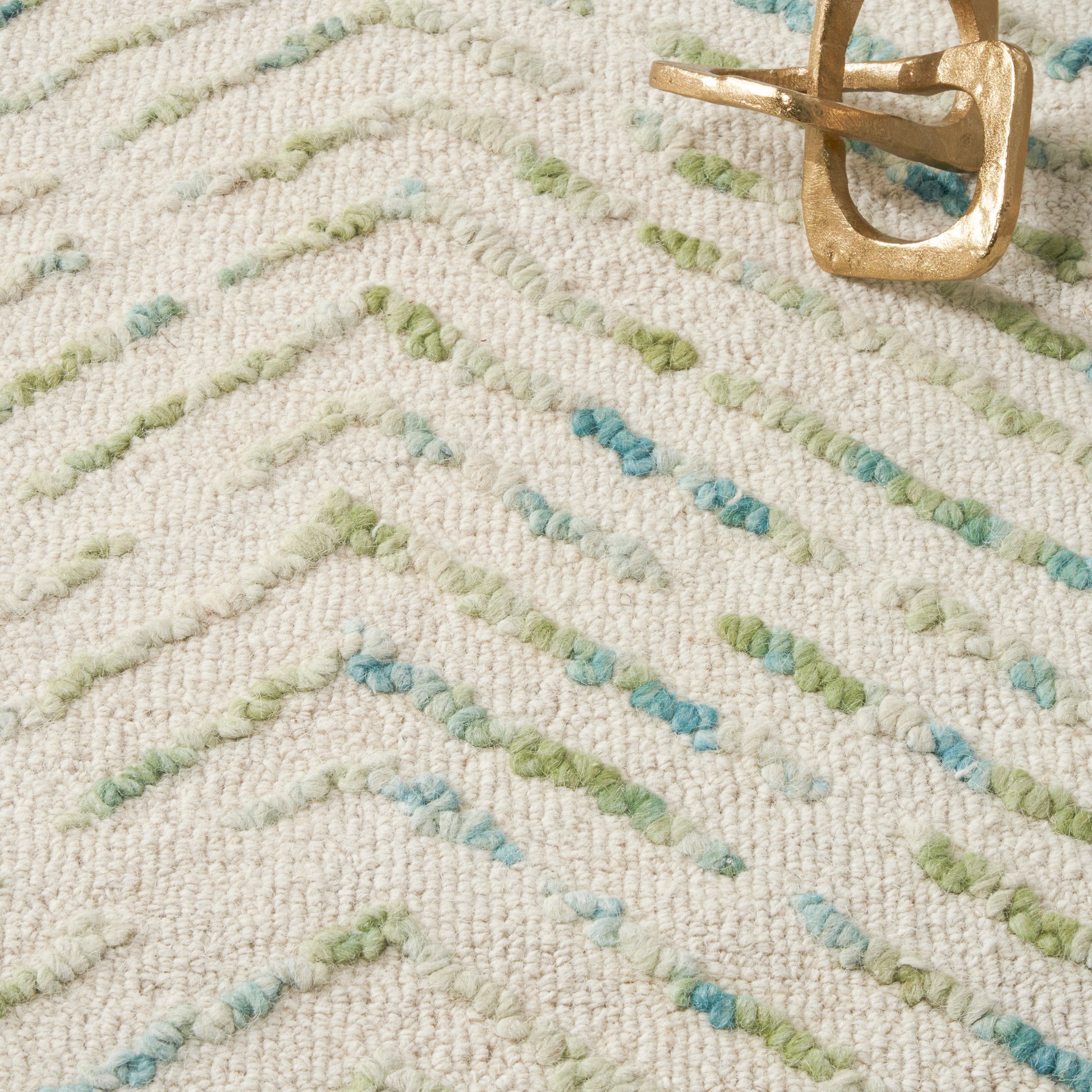 Beige textured area rug with pastel green and blue dashed lines; gold metal belt buckle on top.